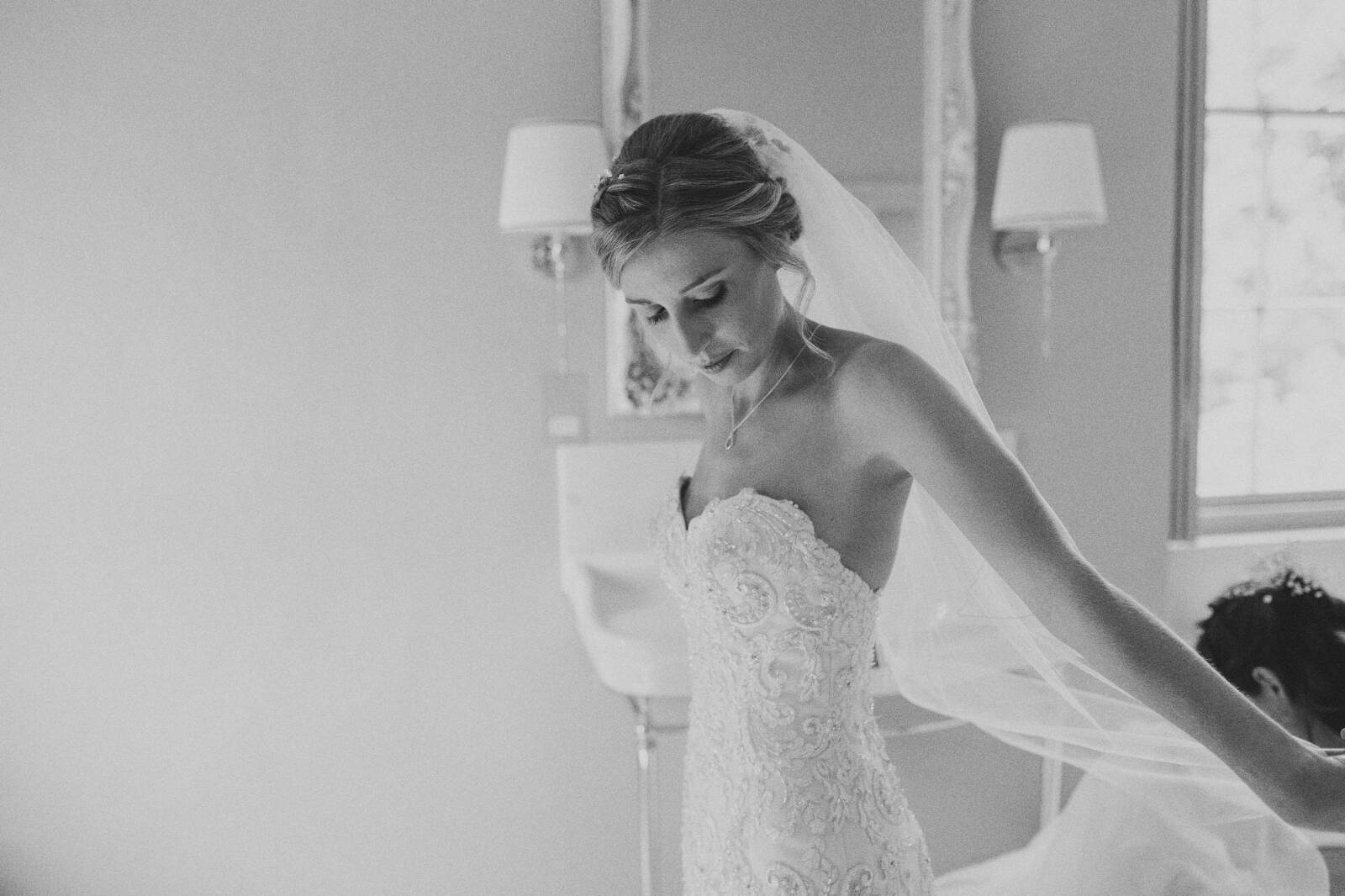 black and white shot of bride putting on wedding dress